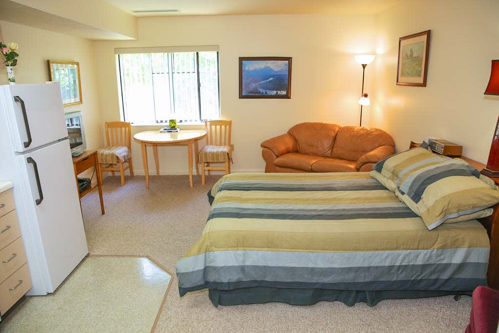 A cozy bedroom with a bed, sofa, and dining area by the window.