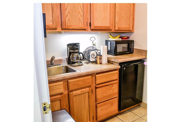 A compact kitchen with wooden cabinets, featuring a coffee maker and microwave on the countertop.