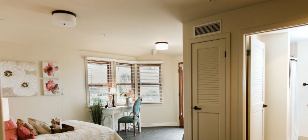 A cozy bedroom with a desk and chair by the window, featuring warm lighting and inviting decor.