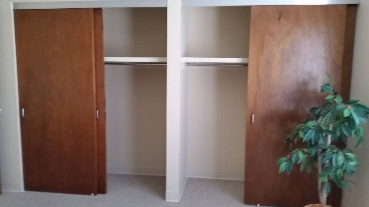 An empty closet with wooden sliding doors, featuring shelves and hanging space.