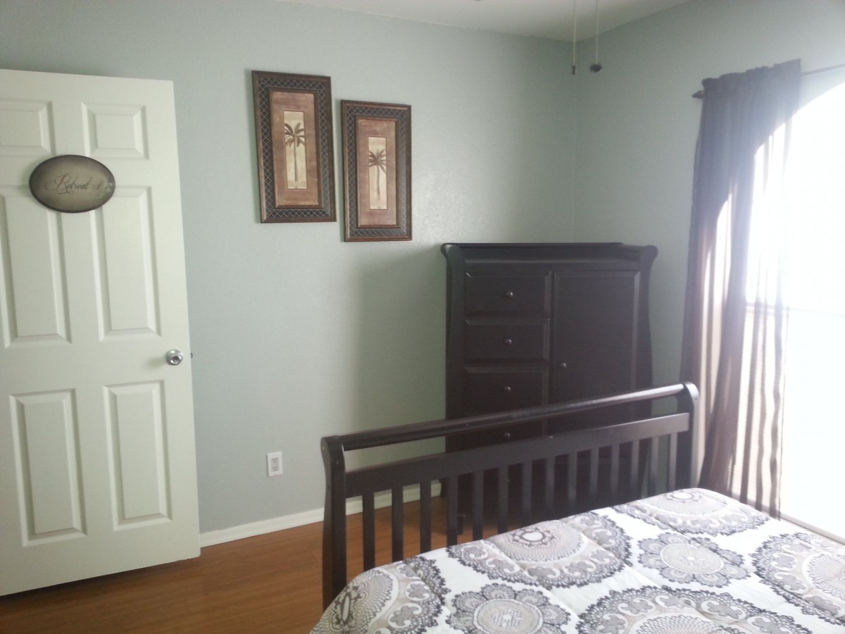 A neatly arranged bedroom with a bed, dresser, and wall art.