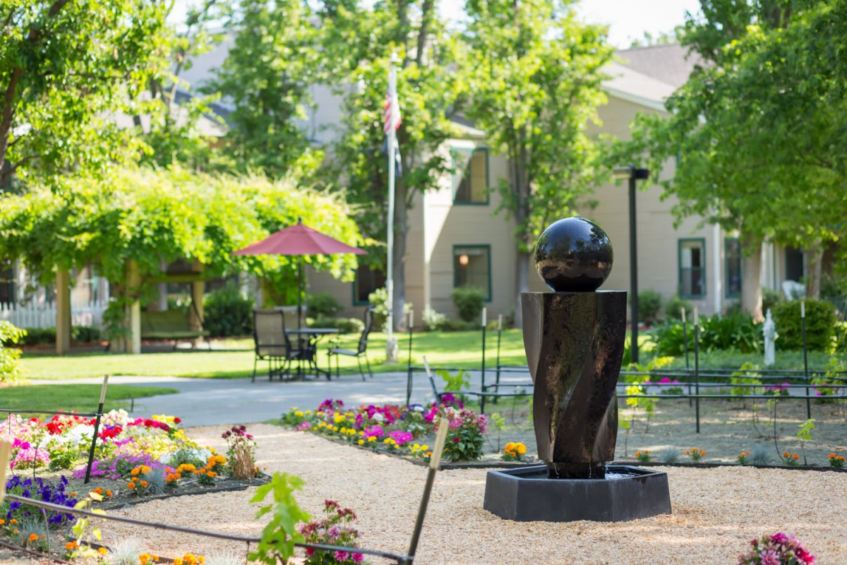A scenic garden area with a sculpture, surrounded by flowers and trees.