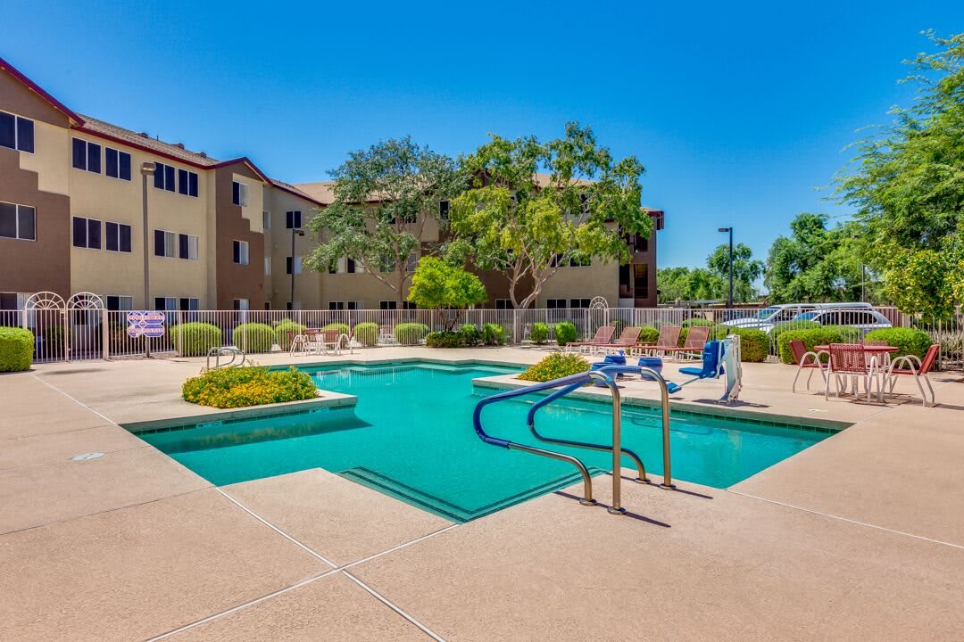 A sunny day at a residential apartment complex with a swimming pool surrounded by lush landscaping.