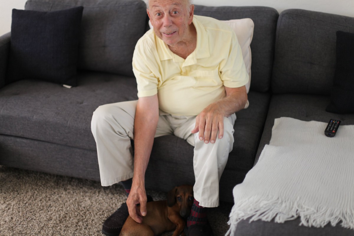 An older man sitting on a couch, petting a small dog.
