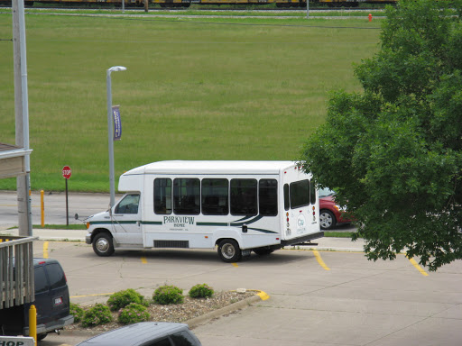 A white shuttle bus parked in a parking lot with a green field in the background.