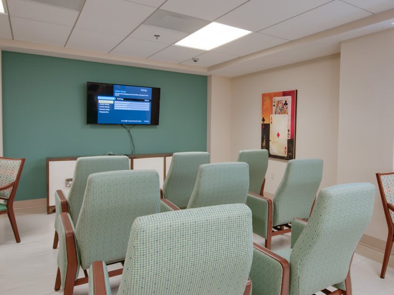 An empty waiting room with arranged chairs and a television on the wall.