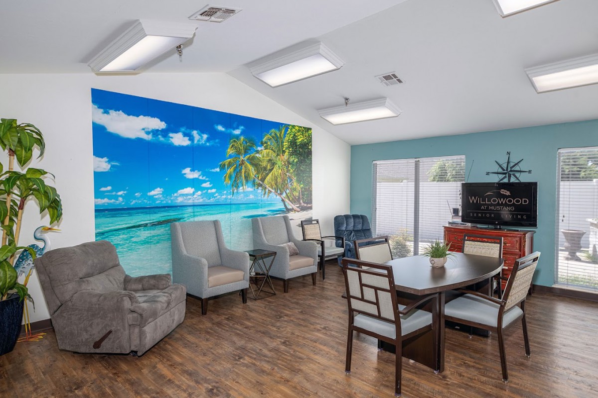 A cozy living room with a beach-themed mural, featuring several chairs and a wooden table.