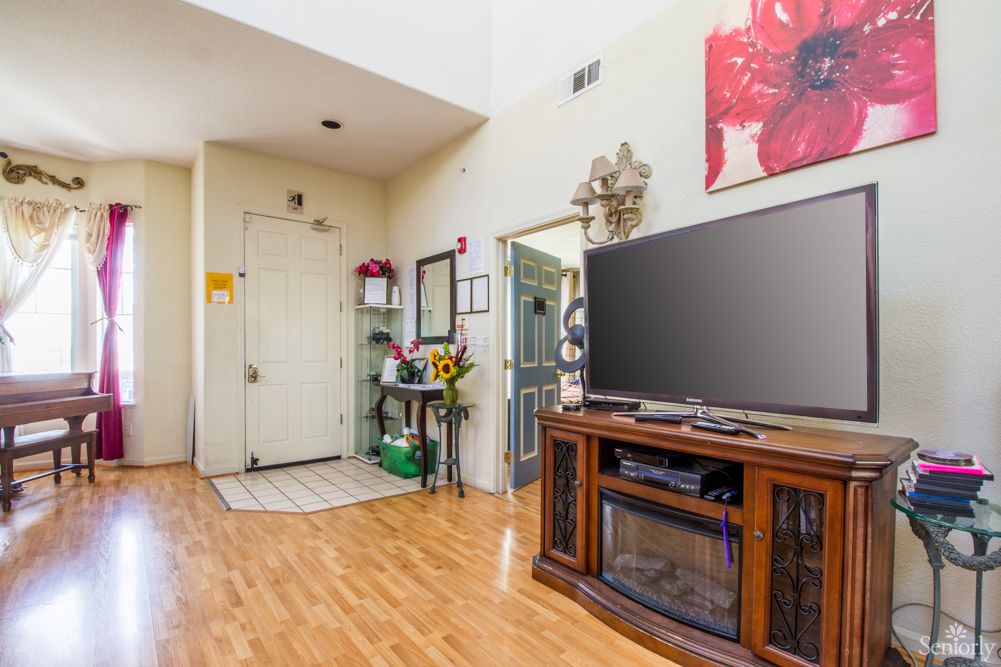 A cozy living room with wooden flooring, featuring a large television and stylish decor near the entryway.
