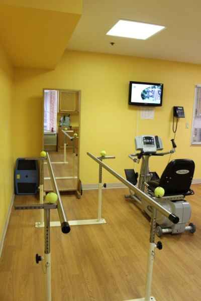 A rehabilitation room equipped with parallel bars, a stationary bike, and a mirror for physical therapy.