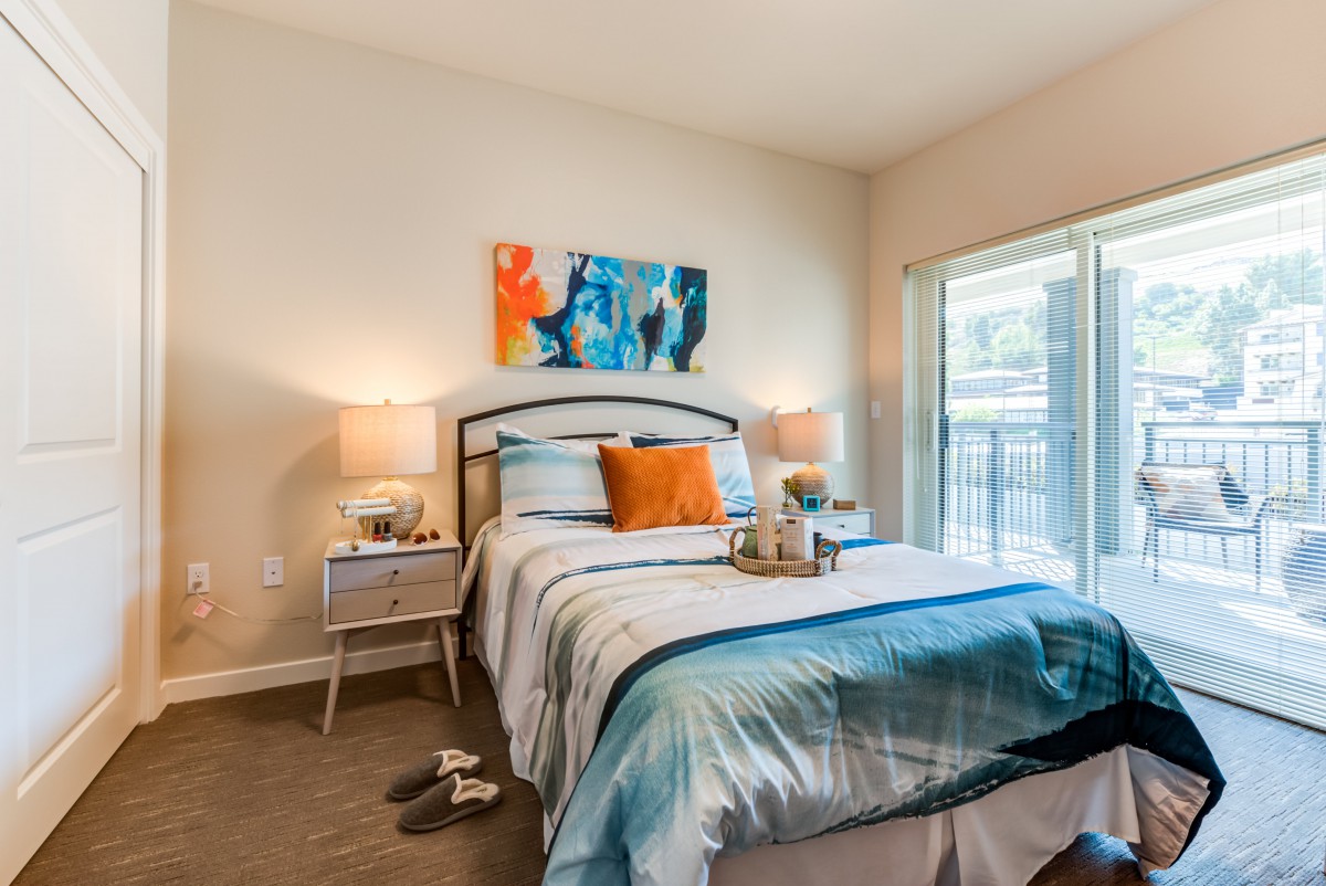 A modern bedroom with stylish decor, featuring a bed with blue and orange accents, bedside lamps, and contemporary artwork.