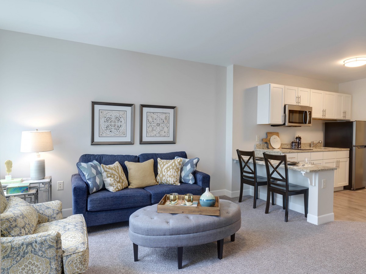 A modern, cozy living room with a blue sofa and open kitchen layout.