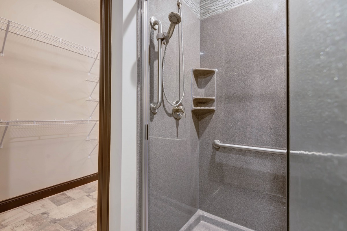 A modern shower with a handheld showerhead, built-in shelves, and a grab bar in a tiled bathroom.