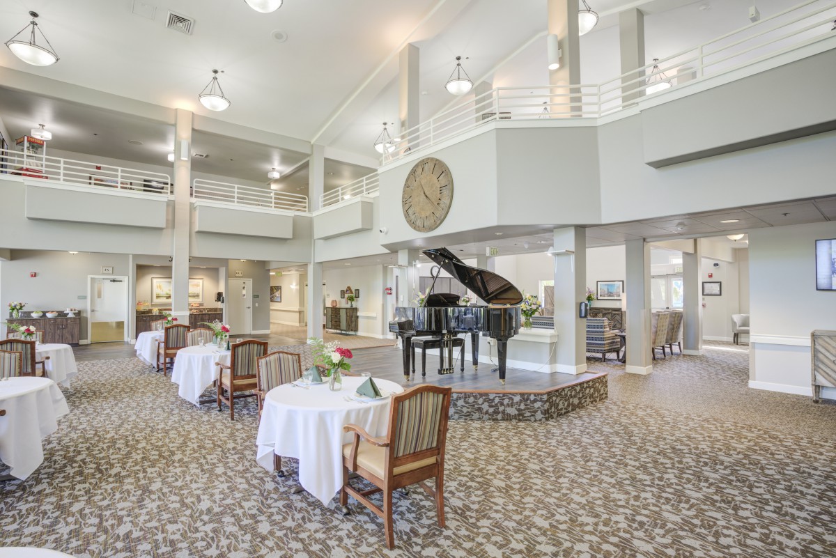 A spacious and elegant dining area featuring a grand piano, with tables set and chandeliers overhead.