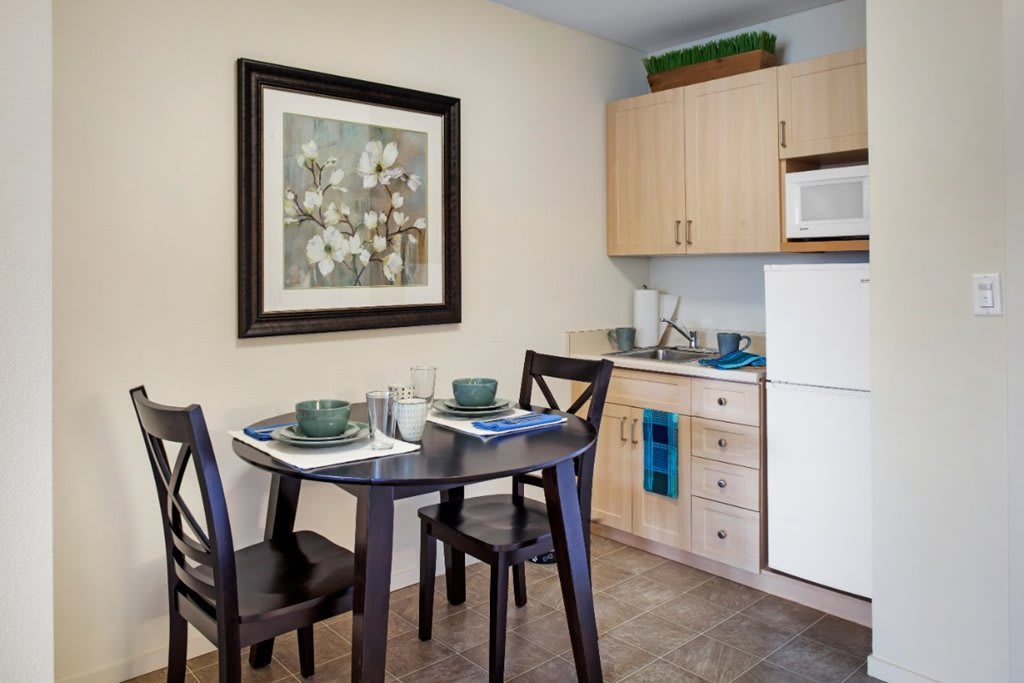 A cozy kitchen corner with a small dining table set, featuring modern wooden cabinets and appliances.