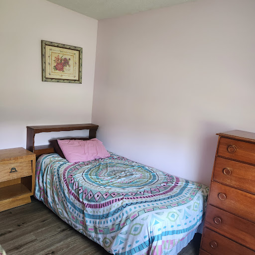 A cozy and simple bedroom featuring a single bed with a decorative blanket and a wooden nightstand.