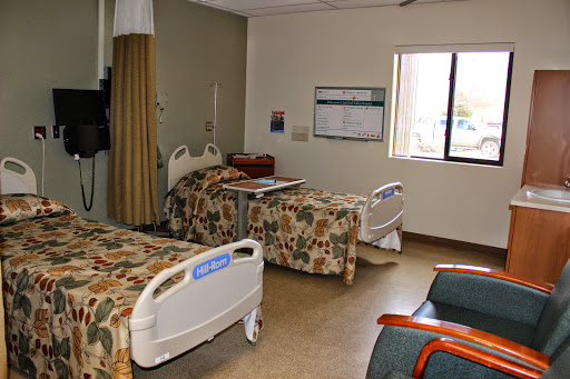 A view of a hospital patient room with two beds and natural light coming from the window.