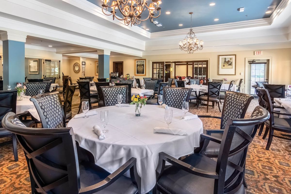 An elegant dining room with neatly set tables and chandeliers.