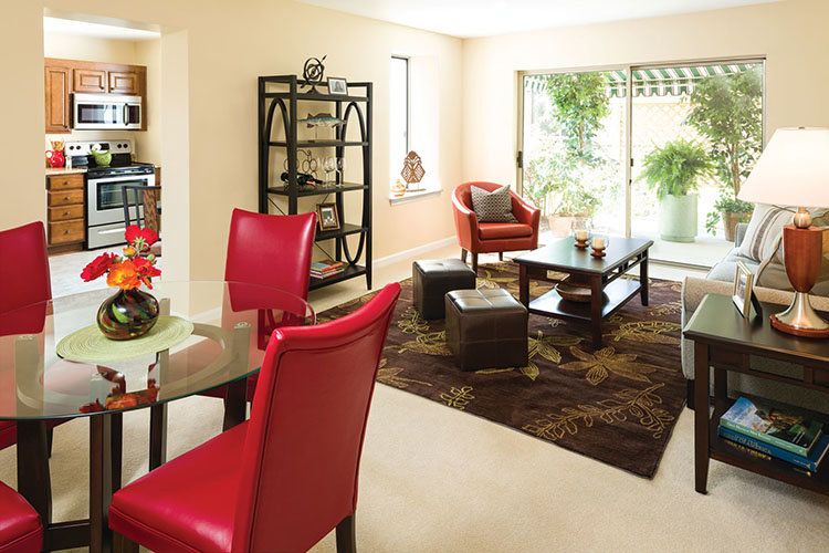 A modern living room with red chairs and a coffee table, featuring ample natural light.
