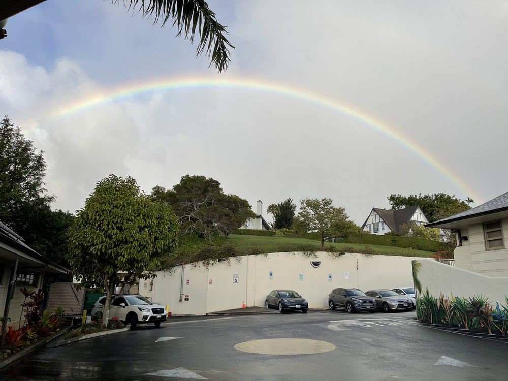 A beautiful rainbow arches over a parking lot on a cloudy day.
