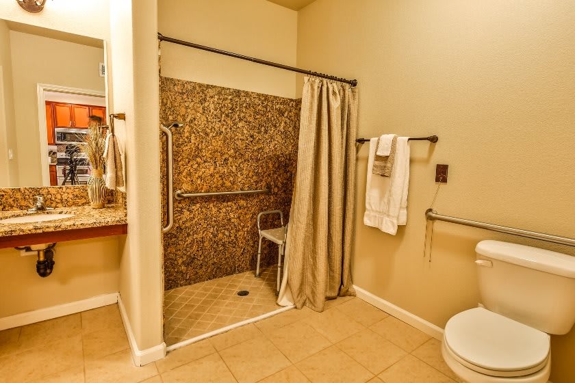 An accessible bathroom with a walk-in shower, grab bars, and a towel rack.
