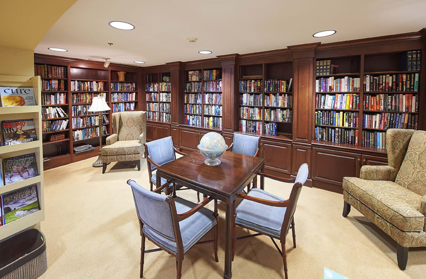 A cozy library reading room with wooden bookshelves, a table, and chairs.