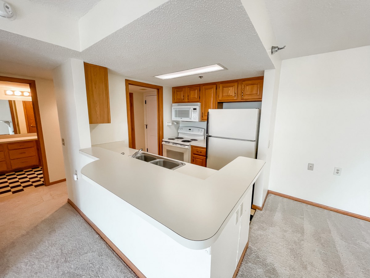 A modern kitchen with white appliances and wood cabinets in an apartment.