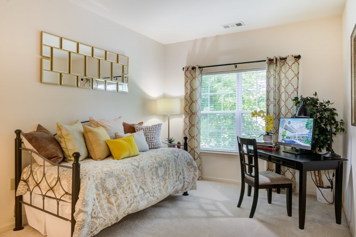 A cozy bedroom with a bed, decorative pillows, a desk, and a large window with curtains.