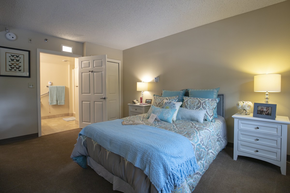 A cozy bedroom with a neatly made bed in light blue tones and soft lighting.