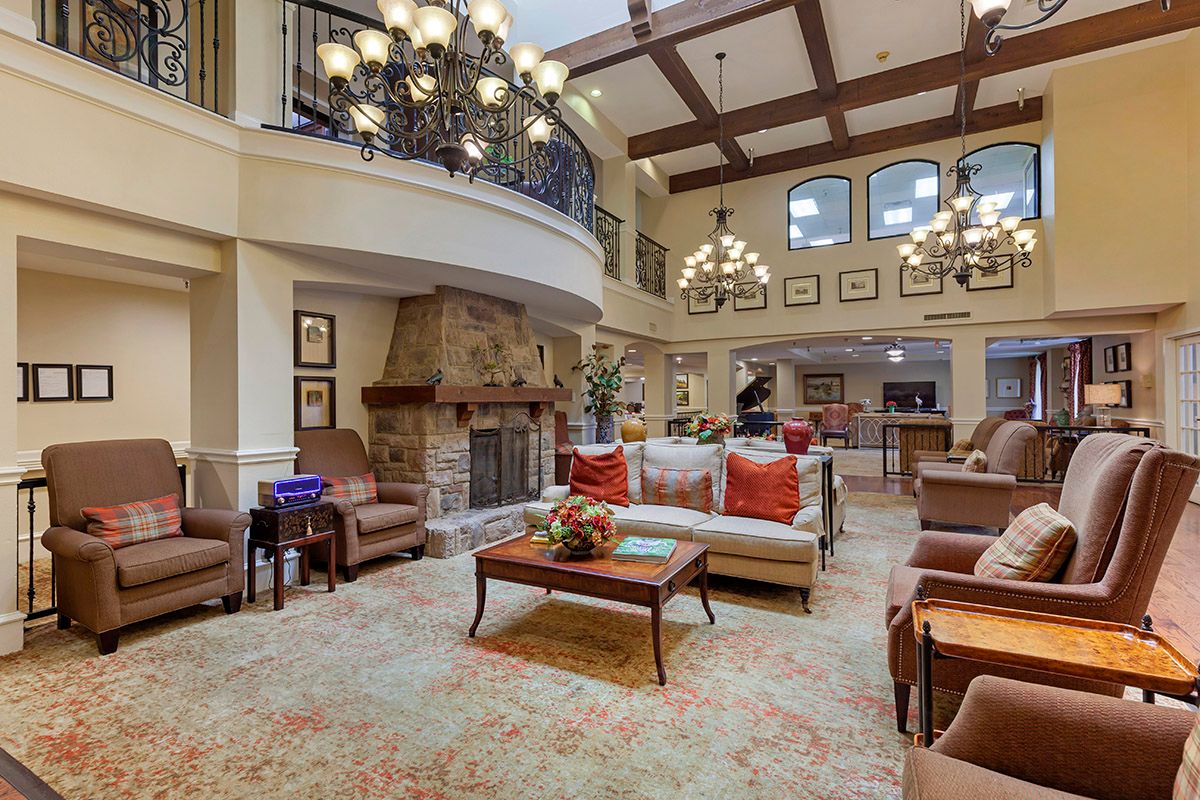 A spacious and cozy living room with elegant chandeliers, comfortable seating, and a stone fireplace.