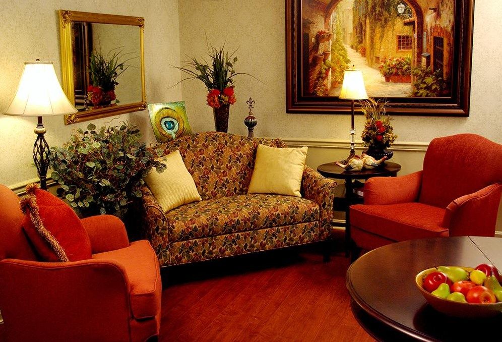 A cozy living room with a patterned sofa, two orange armchairs, and a warmly lit table lamp.