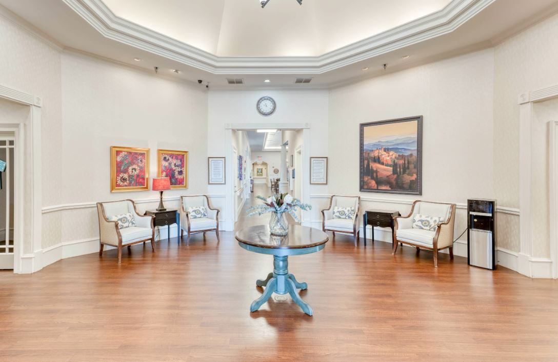 A well-lit lobby or waiting area with chairs arranged along the walls, featuring a central table and decorative artwork on the walls.