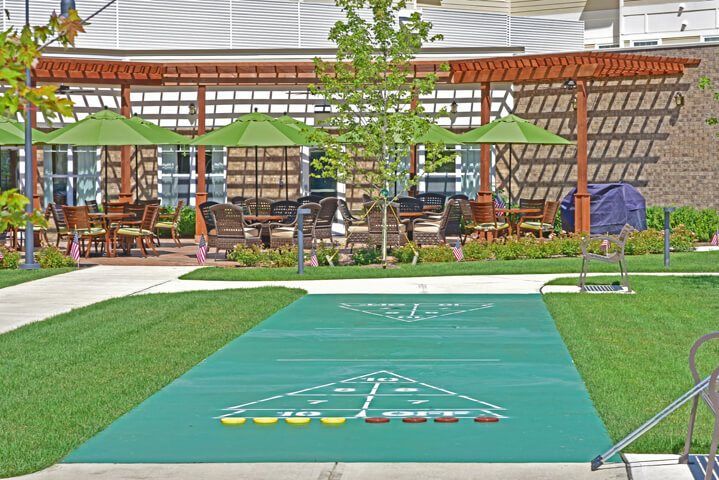 An outdoor recreation area featuring a shuffleboard court surrounded by patio furniture and greenery.