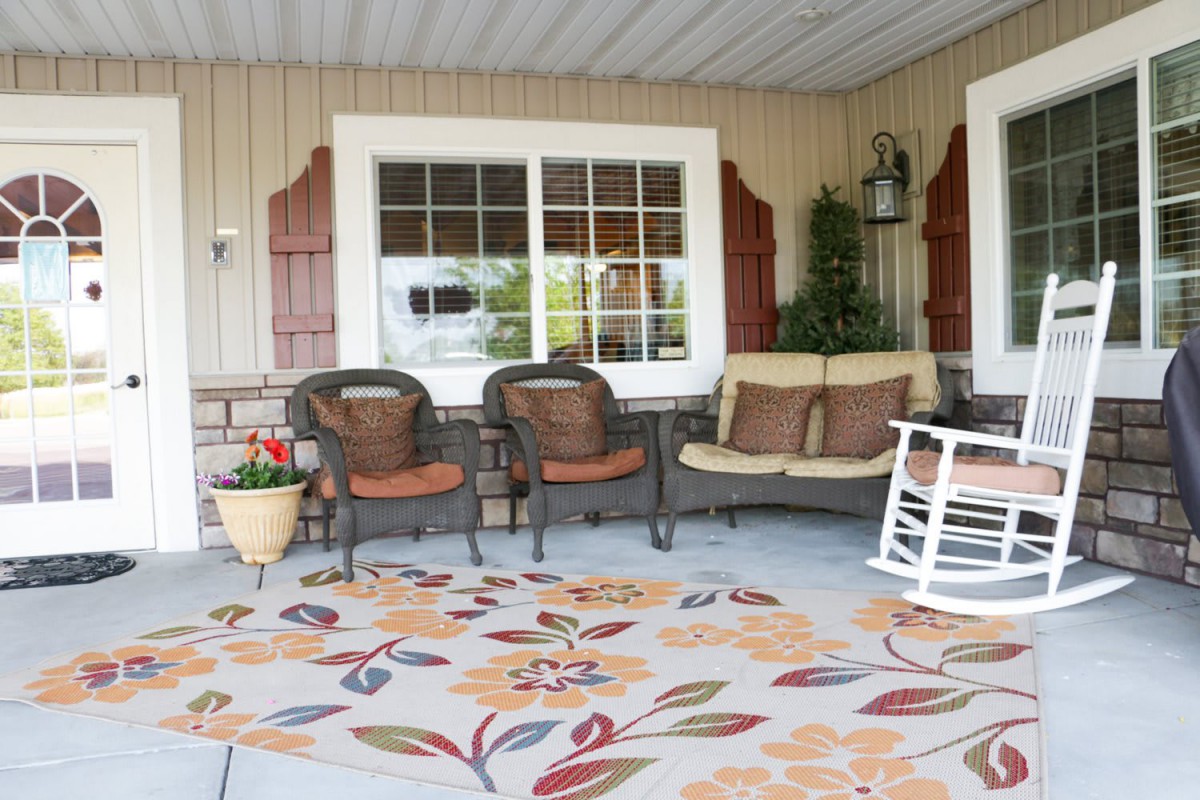 A cozy patio setup featuring wicker chairs, a cushioned swing bench, and a rocking chair on a decorative rug.