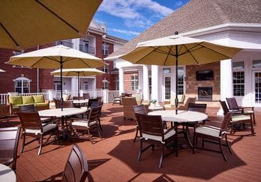 A sunny outdoor patio with tables, chairs, and umbrellas, set against a backdrop of buildings.