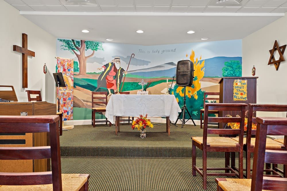 A small chapel with a mural background, altar, and arranged chairs.