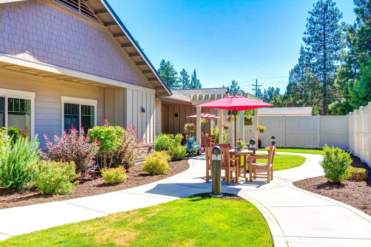 A sunny backyard patio with outdoor furniture and a red umbrella.