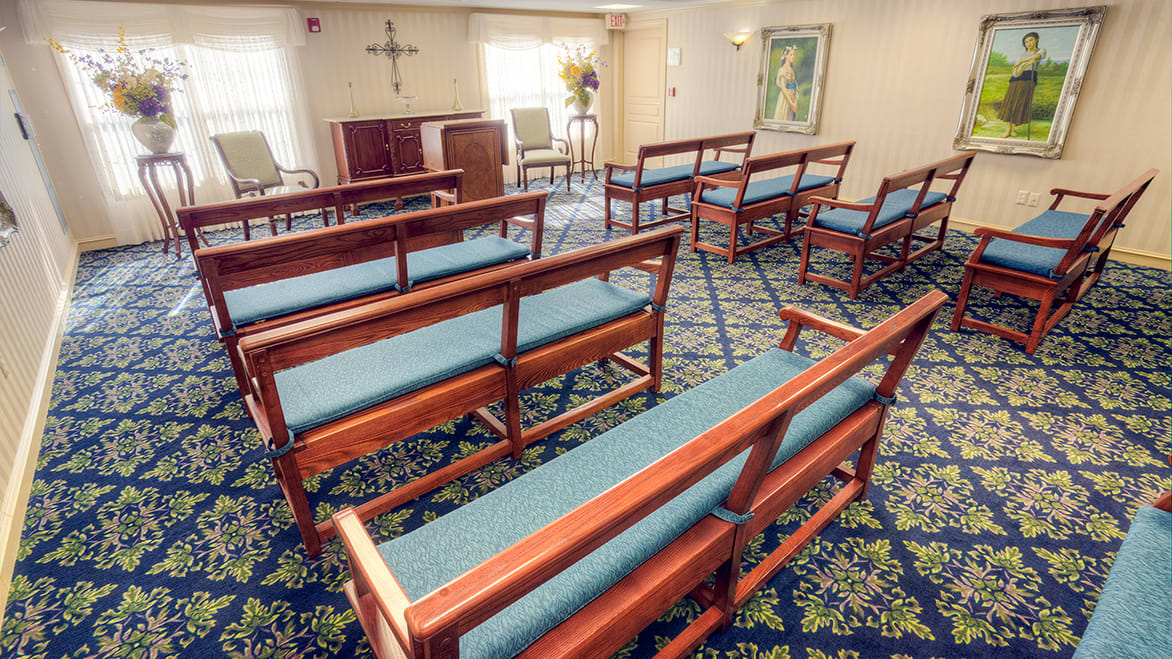 An interior view of a small chapel with wooden pews and a cross on the wall.