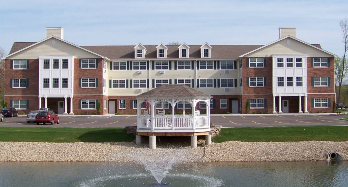 A three-story building with a gazebo in front and a pond with a fountain.