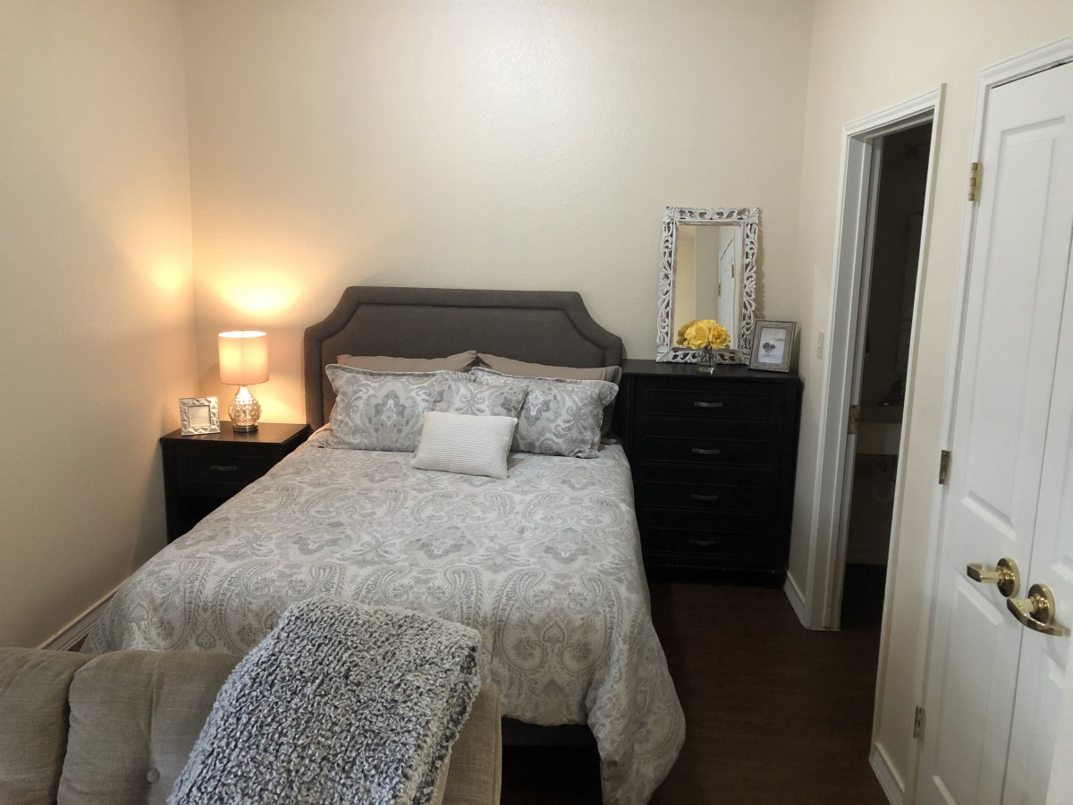 A cozy bedroom with a neatly made bed, bedside lamp, and dresser with a mirror.