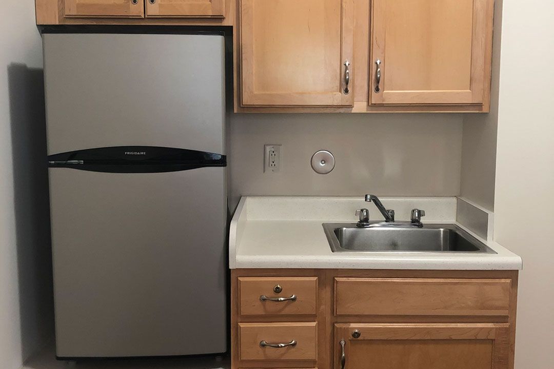 A small kitchen area with a refrigerator, sink, and wooden cabinets.