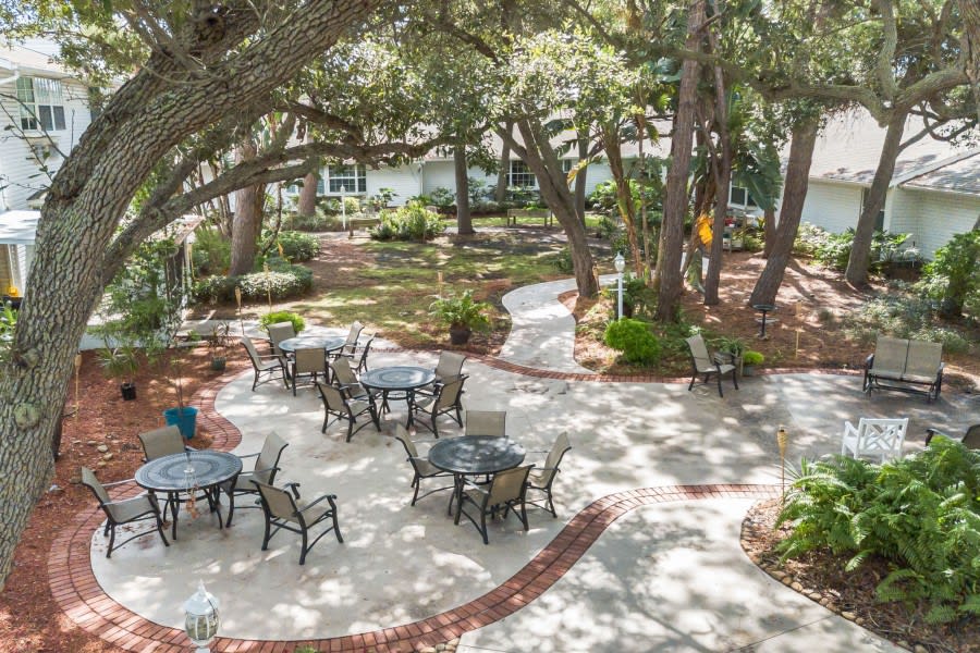 A tranquil outdoor patio area with tables and chairs surrounded by lush greenery and trees.