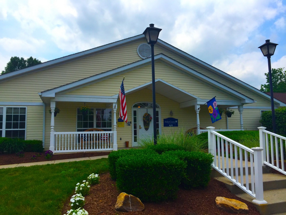A yellow building with a ramp, flanked by American and blue flags, surrounded by well-maintained landscaping.