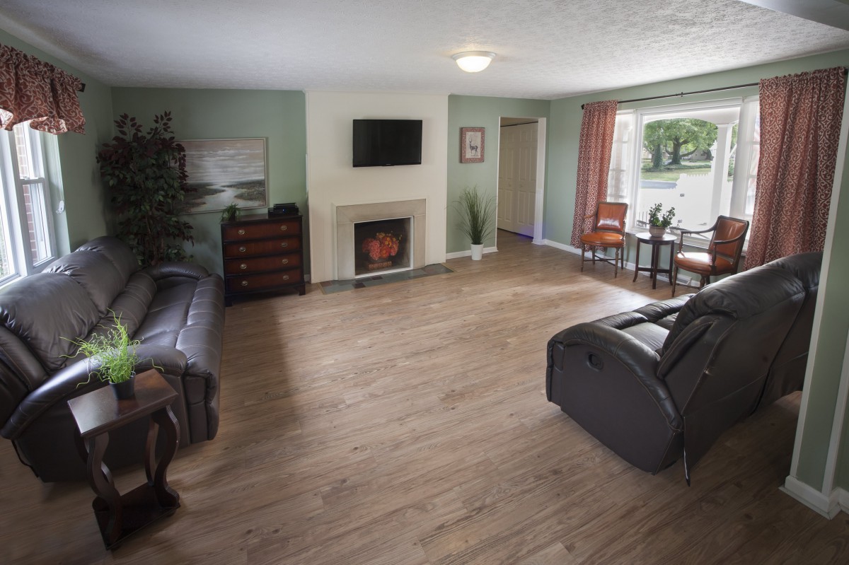 A spacious living room with hardwood flooring, featuring comfortable seating, a television mounted above a fireplace, and a cozy dining area by the window.