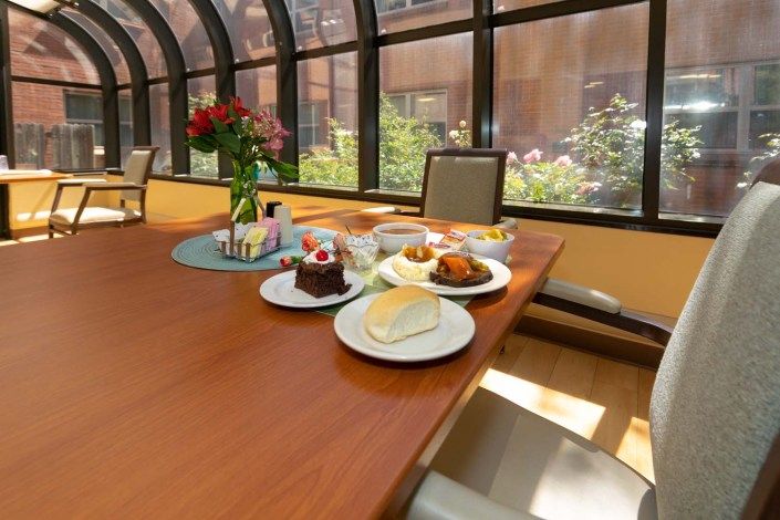 A sunlit dining area with a table set for dessert, featuring various pastries and a vase of flowers.