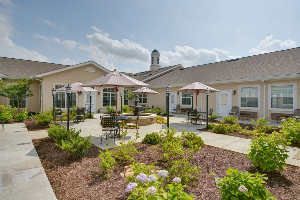 A sunny outdoor patio area with seating and umbrellas surrounded by lush landscaping.