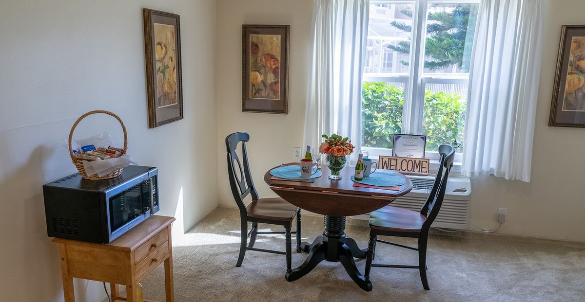 A cozy dining area with a round table and two chairs, bathed in natural light from a large window.
