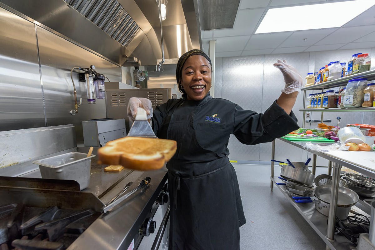 A cheerful chef in a kitchen holding a freshly toasted slice of bread.