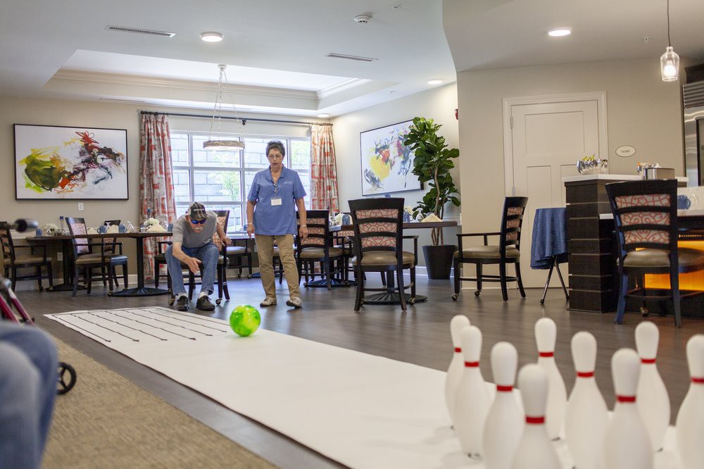 Two people engage in an indoor bowling game, aiming at pins with a green ball.