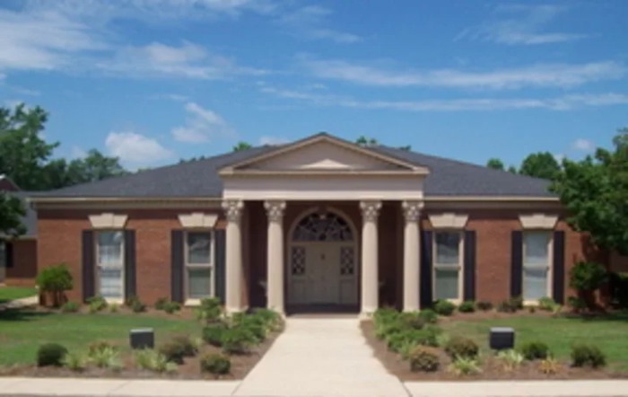 A classical-style brick building with columns and a neatly landscaped front yard.