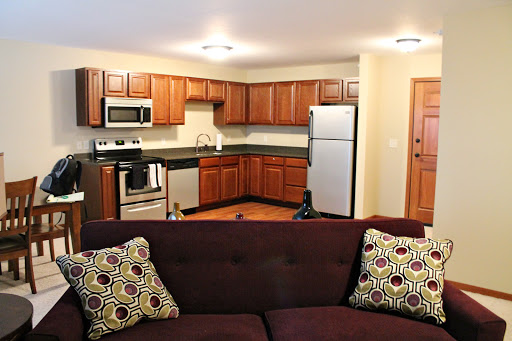 A cozy, modern kitchen and living room setup featuring wooden cabinets, stainless steel appliances, and a comfortable sofa.